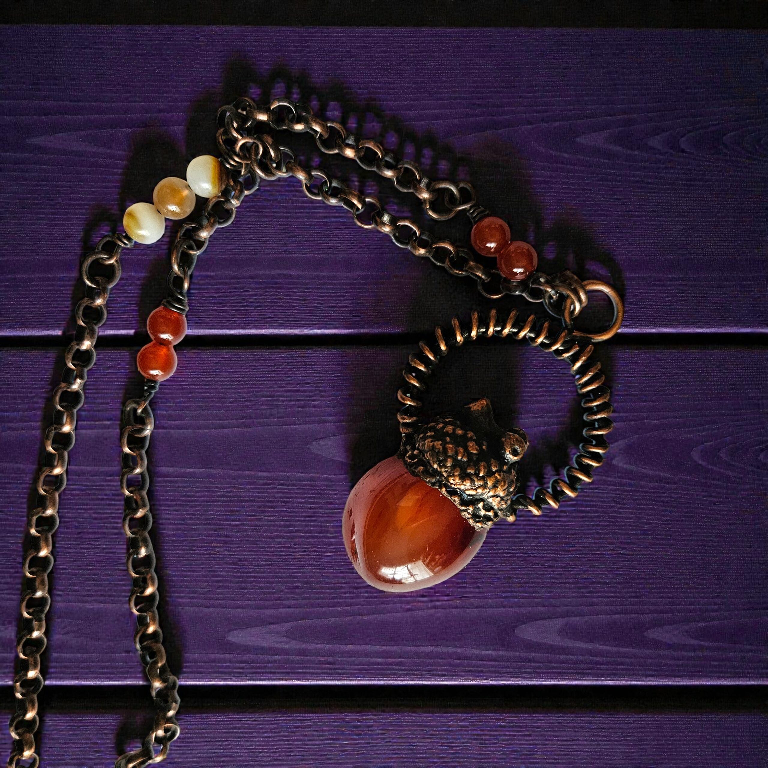 Close-up view of the intricate copper textures on the acorn cap and the hand-forged wire-wrapped halo encircling the polished carnelian stone.