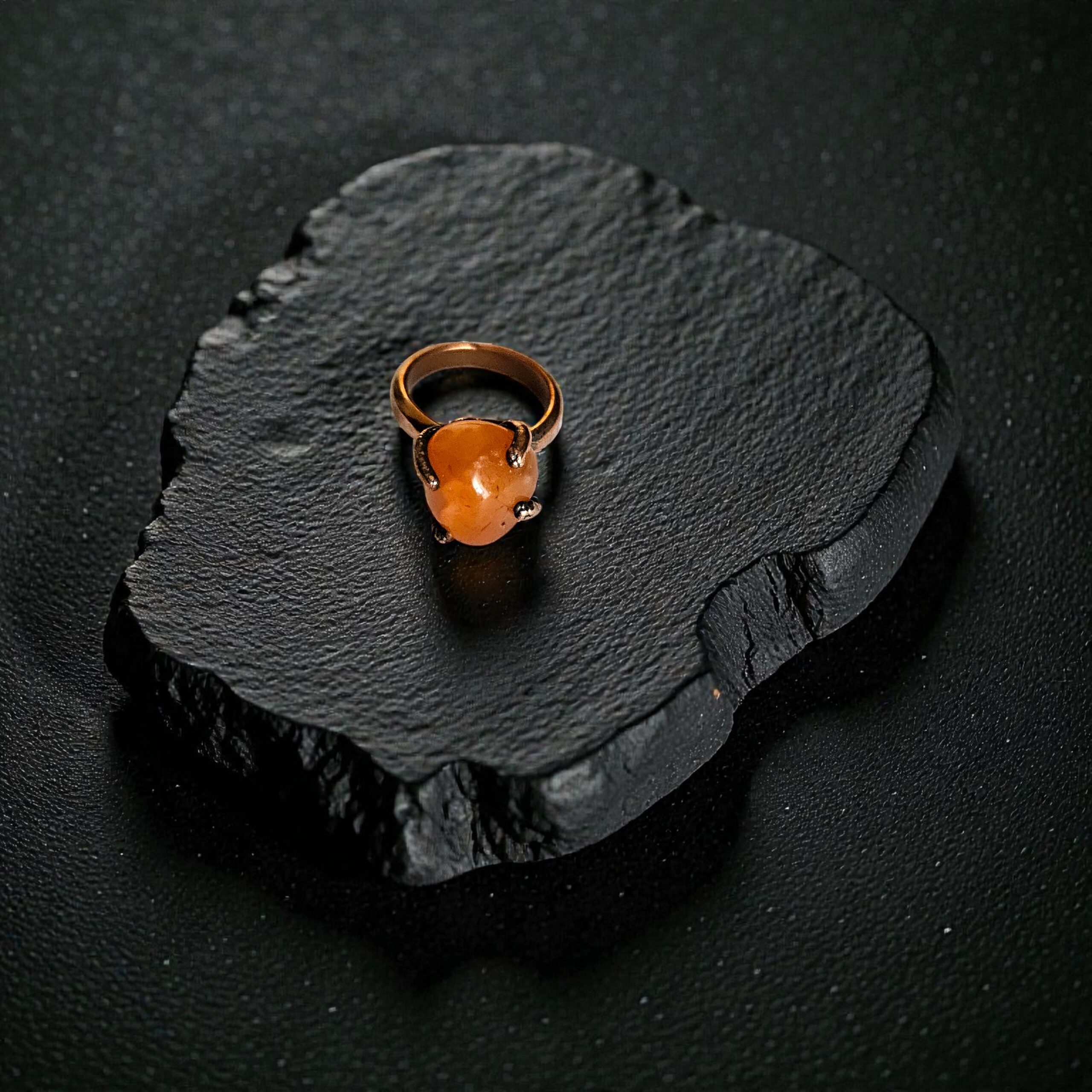 Top-down view of a deep orange carnelian ring set in a rustic, dark-patina copper electroformed setting.