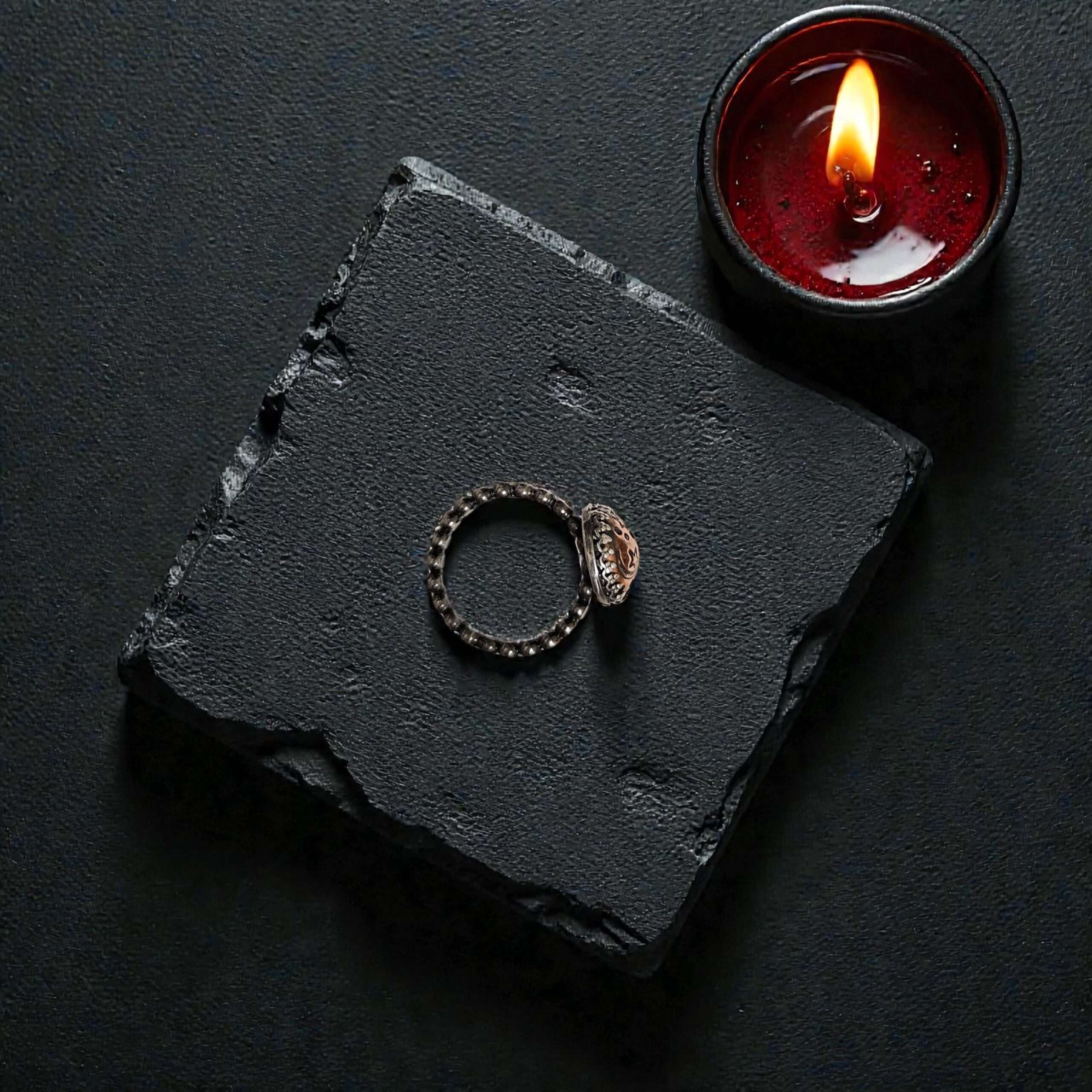 Top-down view of a copper talisman ring on a black stone next to a red candle, highlighting its ancient signet vibe.