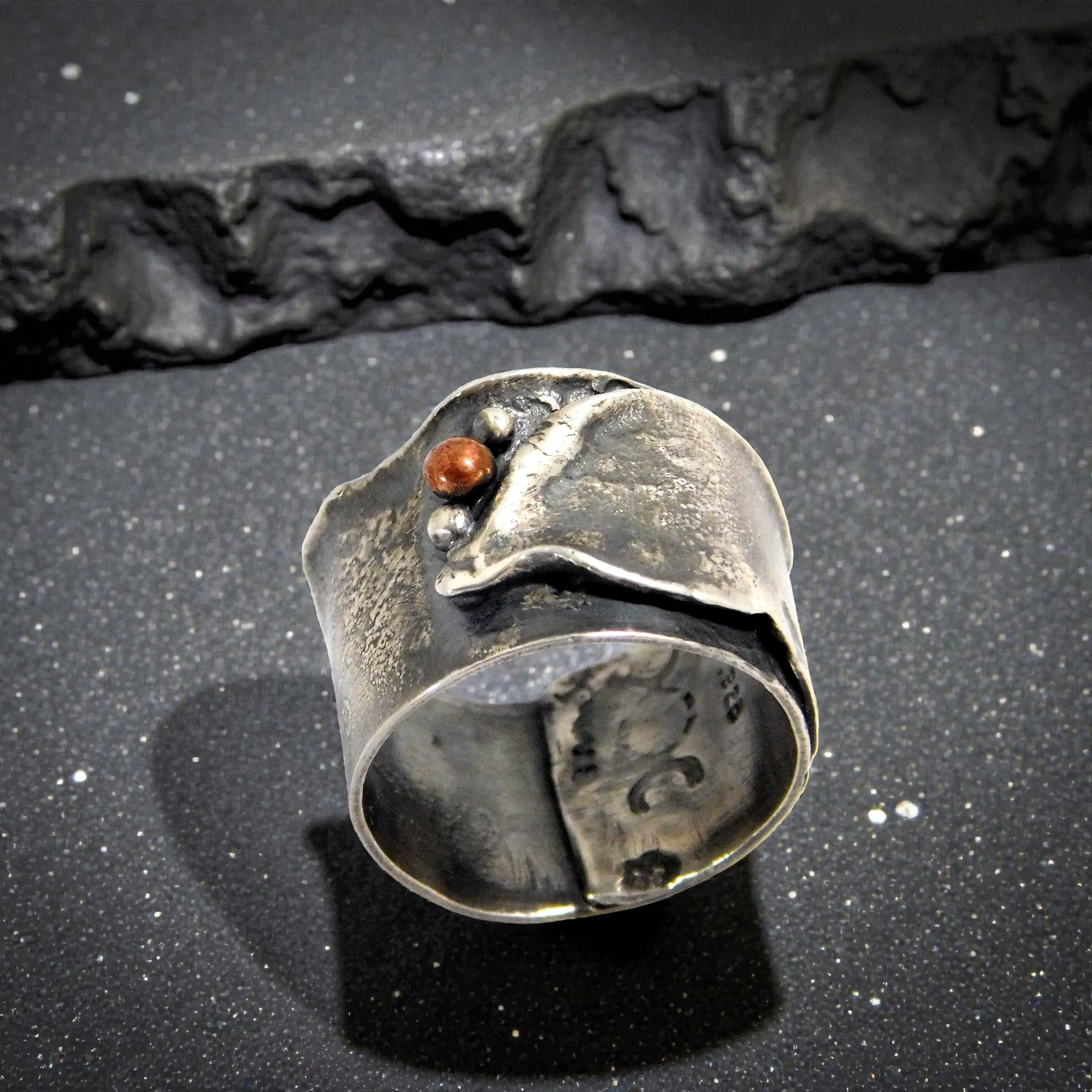 A rugged, ancient-style sterling silver moon ring with mixed metal copper accents on a rustic background