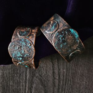 Hand-forged copper Triple Moon cuffs with a midnight blue patina on a background of dark wood and purple velvet.