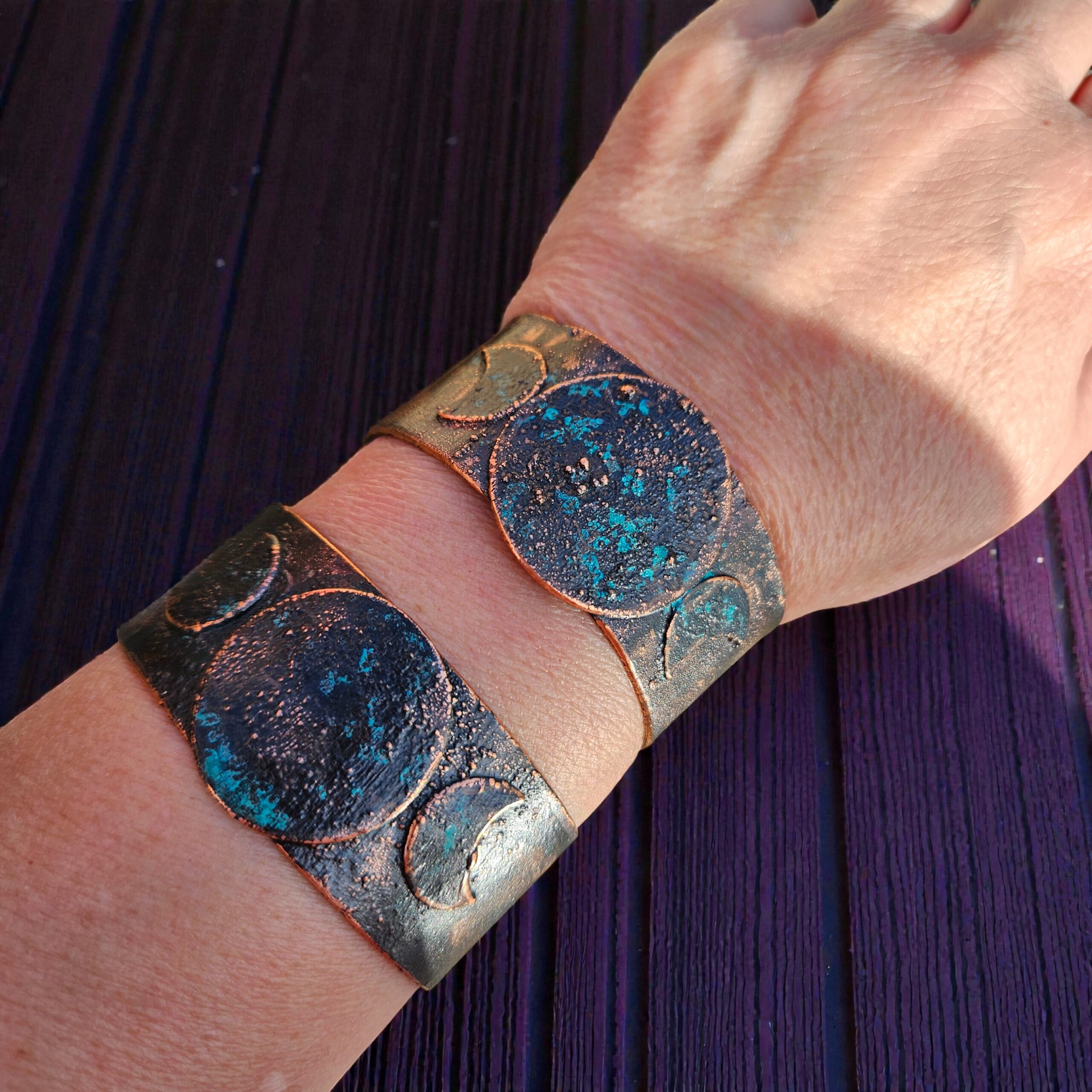 Wide-band copper Triple Moon cuff with blue patina worn on a wrist, showcasing the gnarled texture and artisan craftsmanship.