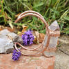 Hand-forged copper Archeron Cuff with a large vertical quartz point, displayed outdoors with lavender and stones.