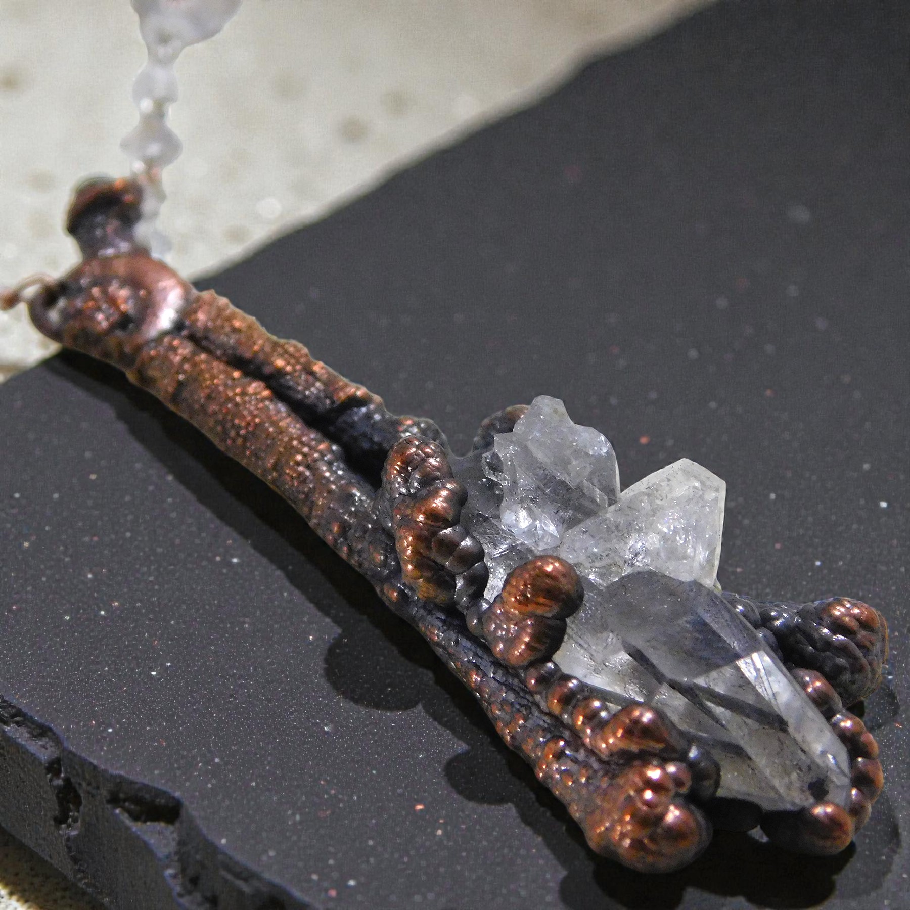 Close-up of "The Sticks and Stones" pendant showing the detailed copper-plated boxwood branches and a multi-point master healer quartz crystal.