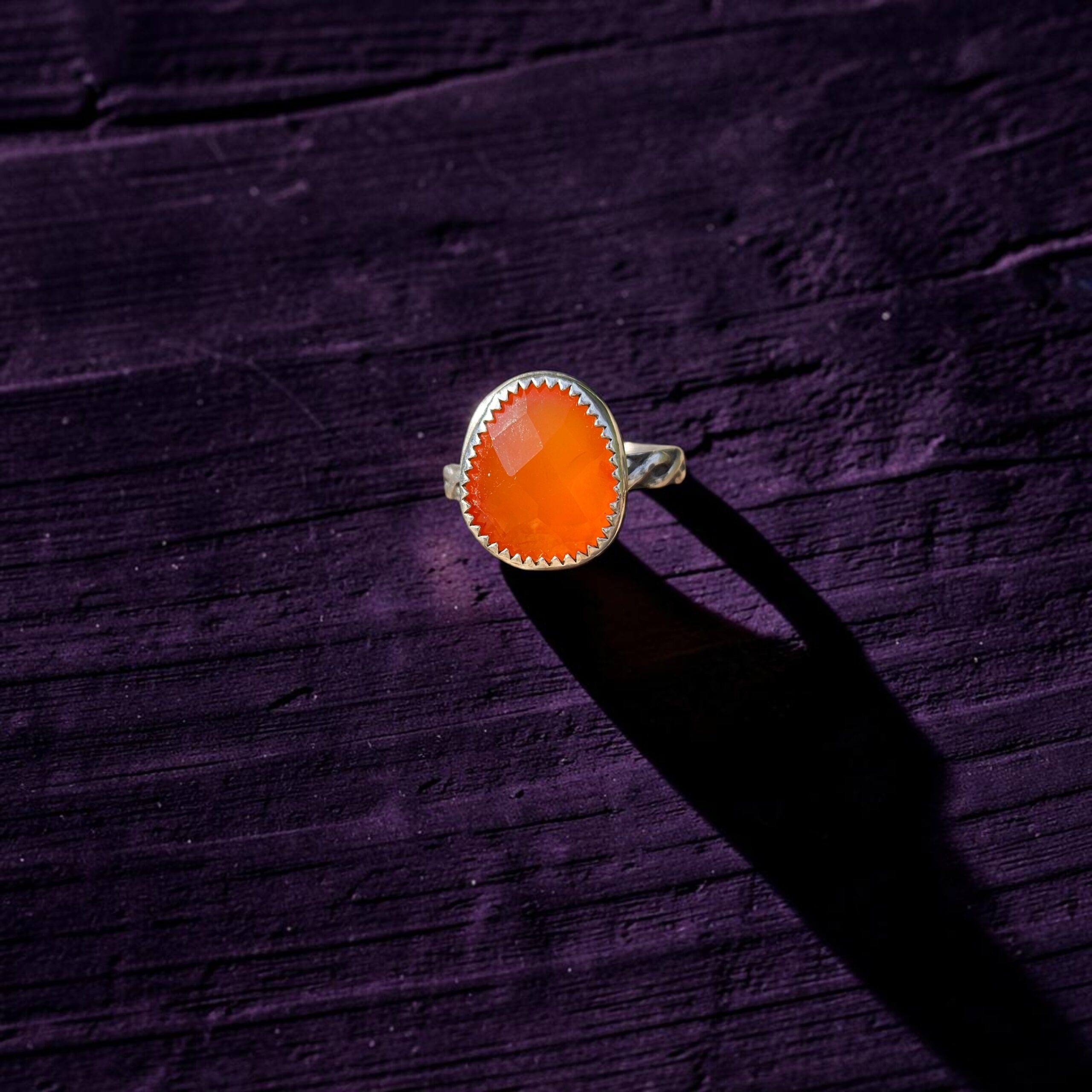 Close up view of a rosecut carnelian ring set in sterling silver on a dark purple wood background