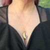 A hand-fabricated copper moon pendant with a blue-flash Labradorite gemstone, worn on a delicate gold chain.