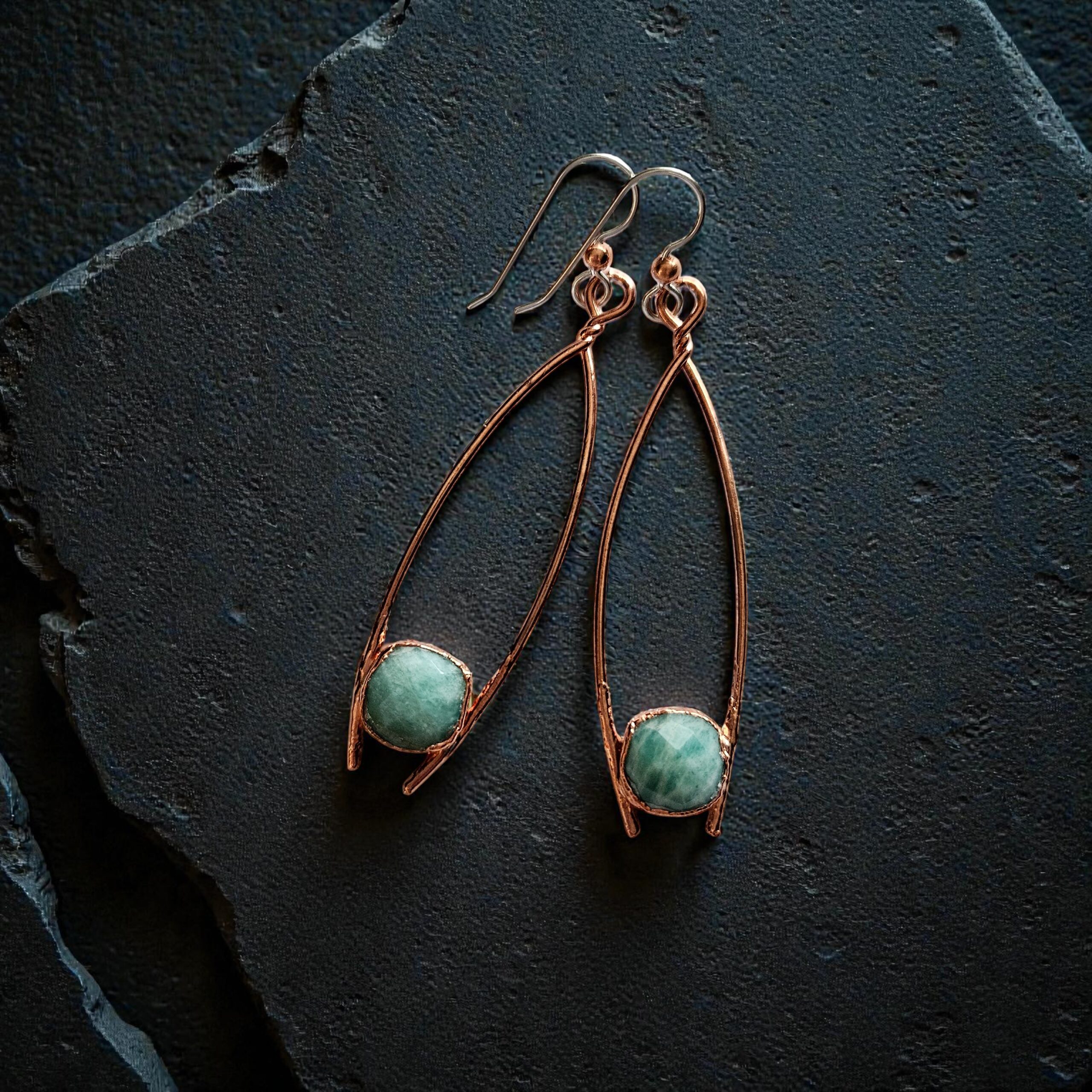A pair of long copper electroformed earrings featuring raw blue-green aquamarine crystals on a dark, moody background.