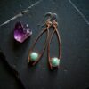 Close-up of the raw aquamarine stones, showing the intricate, dark-patina copper armor and the sterling silver earwire accents.