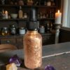The back of the copper-clad bottle shown in an apothecary setting with candles and vintage jars, highlighting the artisan craftsmanship.