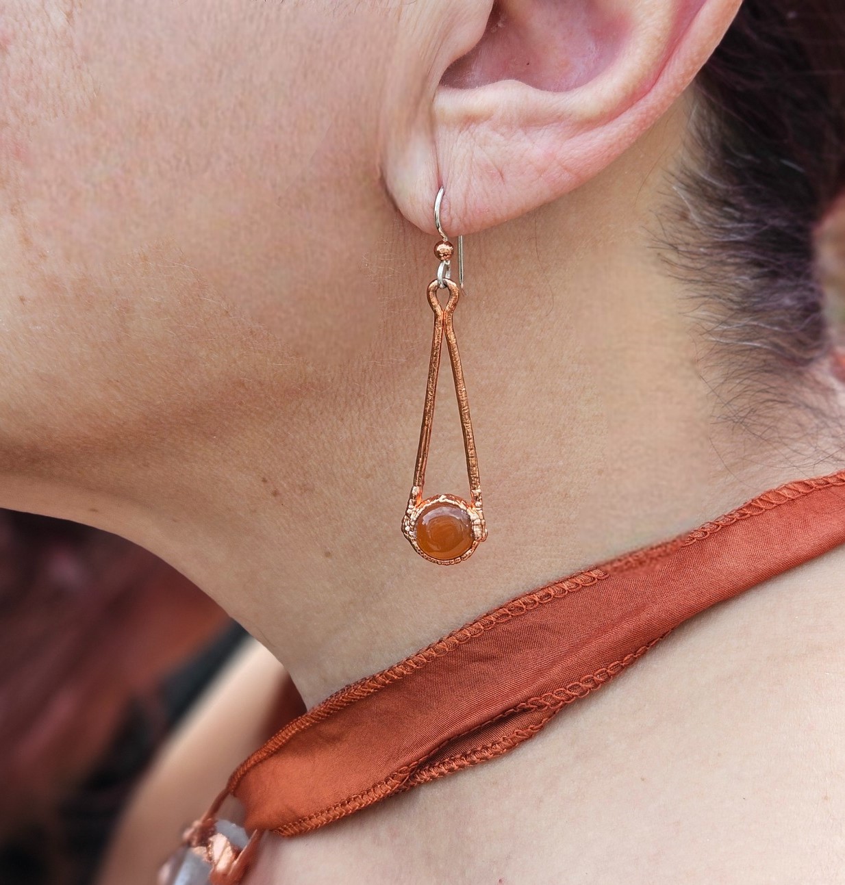 A single carnelian drop earring shown worn, illustrating the 1.5-inch length and the sterling silver earwire against the ear.