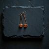 A pair of long copper electroformed earrings with orange carnelian stones resting on a dark, wet slate background.