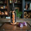 Front view of the Ember Alchemist apothecary bottle featuring three orange carnelian stones set in a vertical copper strip, displayed on a wooden studio table.