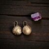 Hand-stamped Merlin's Gold brass earrings with an antiqued celestial moon and star pattern, resting on dark textured wood next to a purple amethyst crystal.