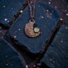 A dark-patina copper electroformed crescent moon amulet featuring a glowing green chalcedony stone.