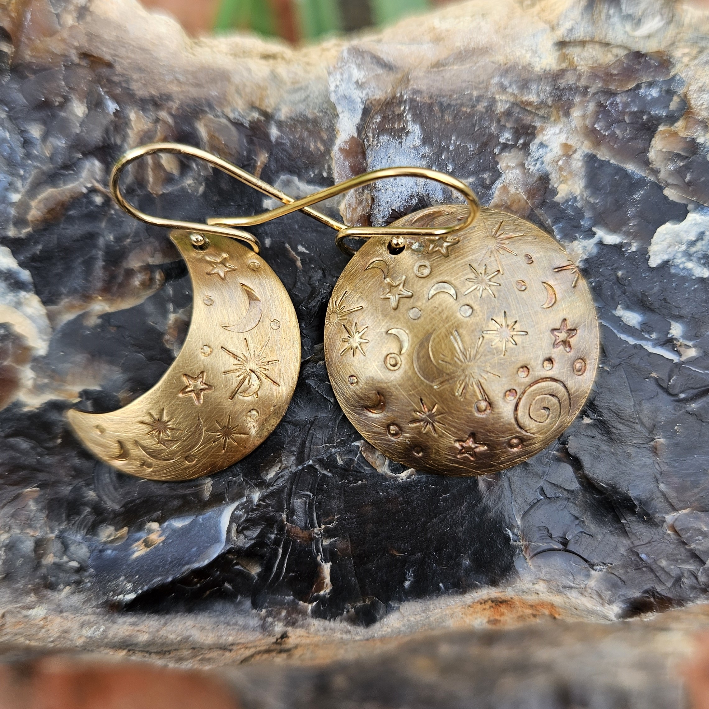 A pair of brass moon phase earrings resting on a natural brown agate stone