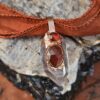 Close-up of a copper electroformed crystal amulet with a large faceted hessonite garnet and a smaller round garnet set into a clear quartz point.