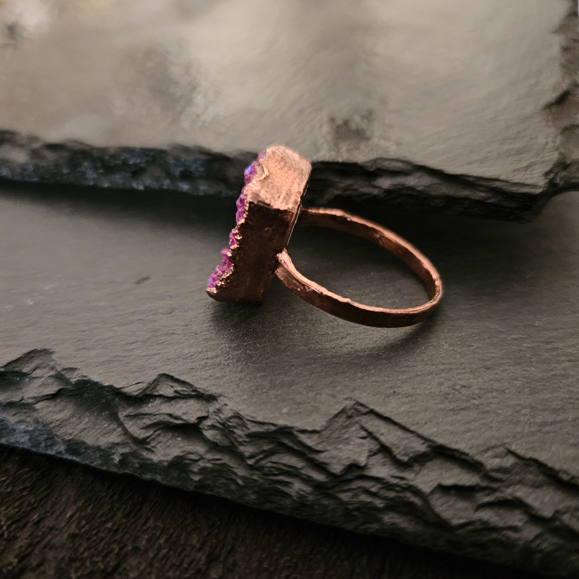 Profile of a hand-sculpted copper ring showing the textured band and the height of the pink druzy setting.