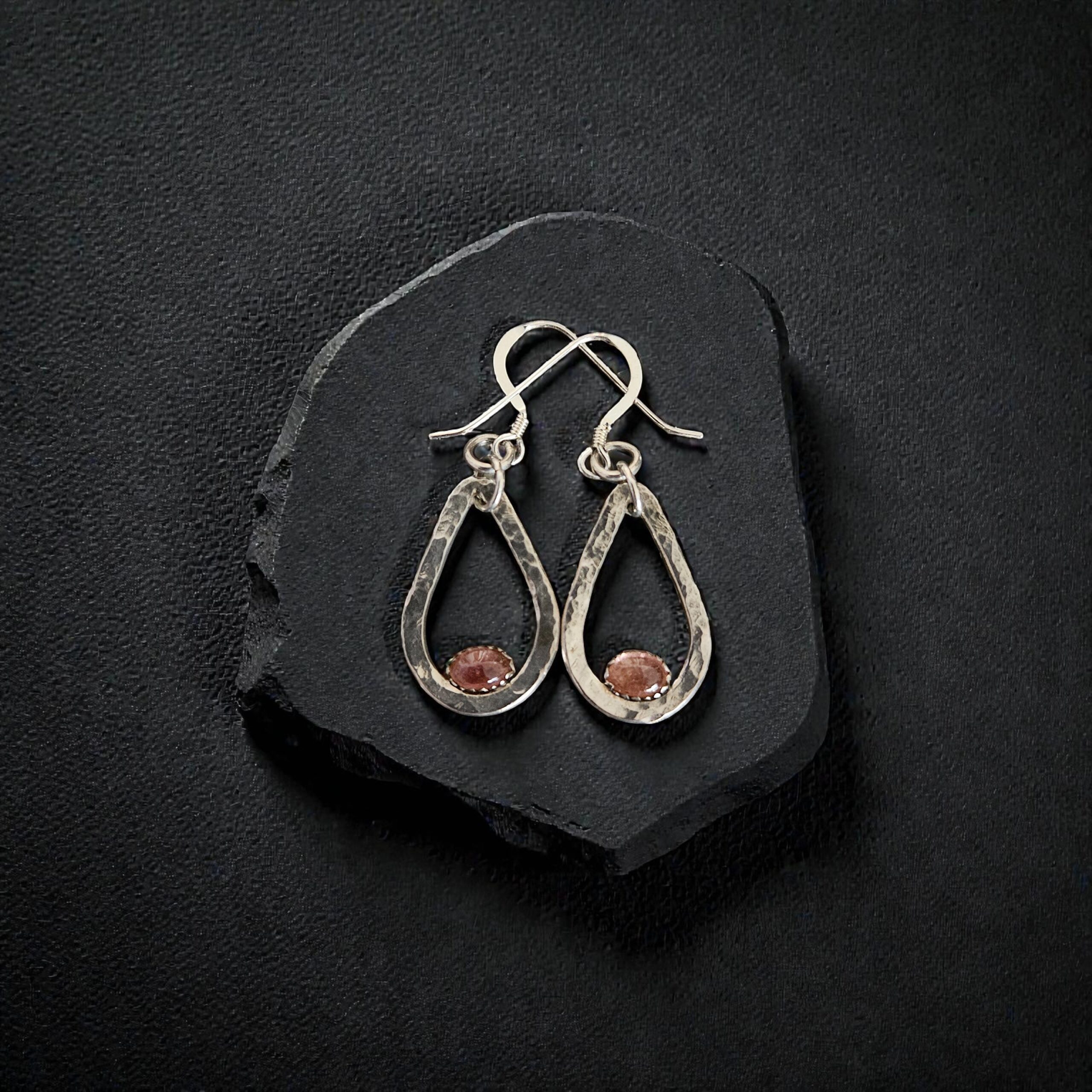Artisan hammered sterling silver earrings with pink tourmaline cabochons displayed on a rugged black slate fragment.