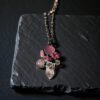 A dark and mysterious pink gemstone cluster pendant displayed on a black slate coaster, highlighting its ancient relic aesthetic.
