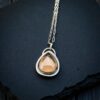 A teardrop-shaped smoky quartz cabochon set in a sterling silver saw-tooth bezel, worn as a pendant on a delicate silver chain.
