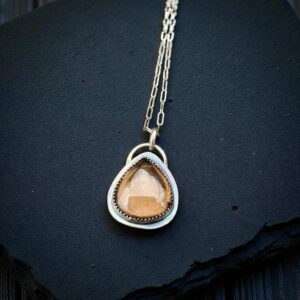 A teardrop-shaped smoky quartz cabochon set in a sterling silver saw-tooth bezel, worn as a pendant on a delicate silver chain.