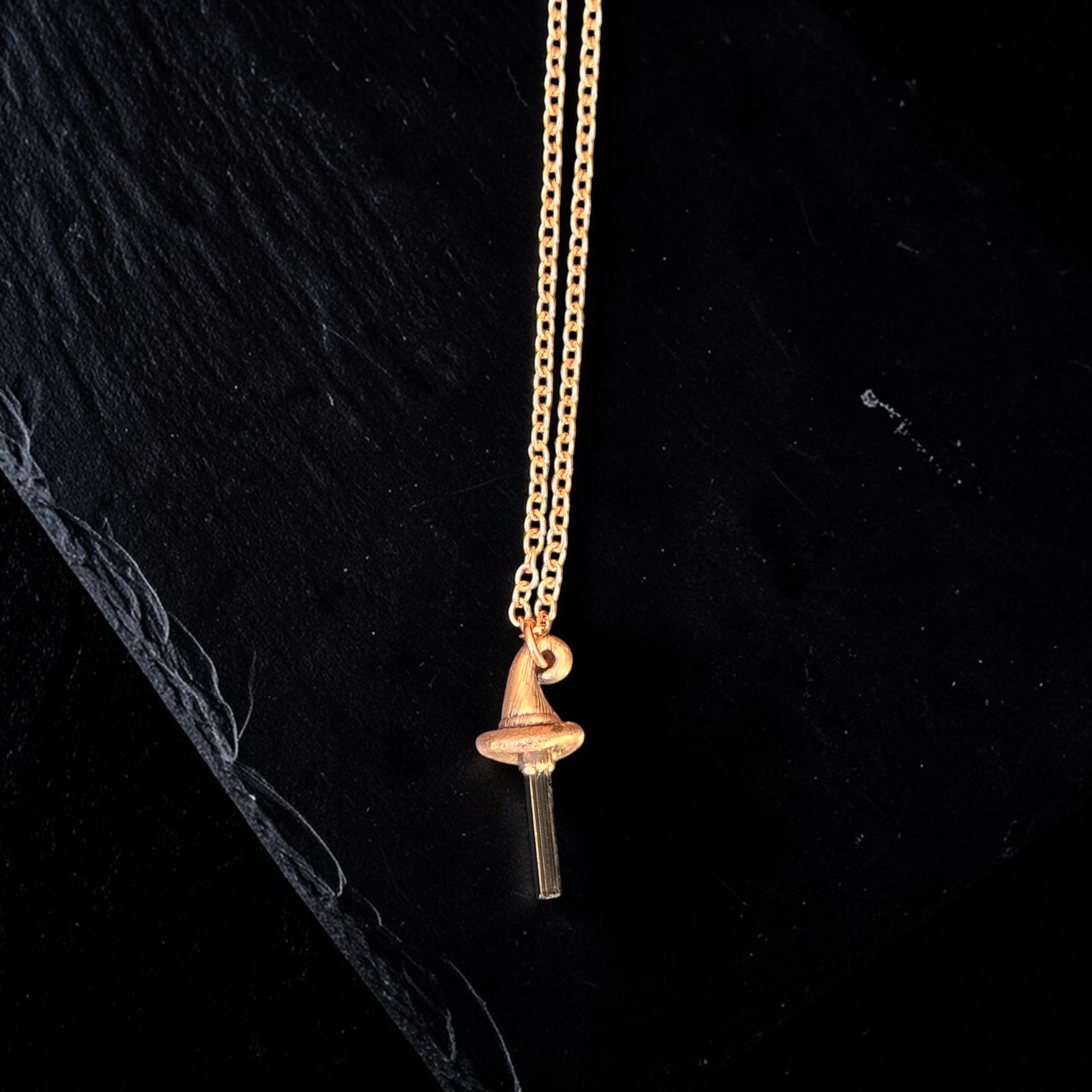 Handcrafted copper electroformed witch hat necklace featuring a raw black tourmaline crystal point as the hat's peak. The pendant hangs from a copper chain against a dark, textured background.