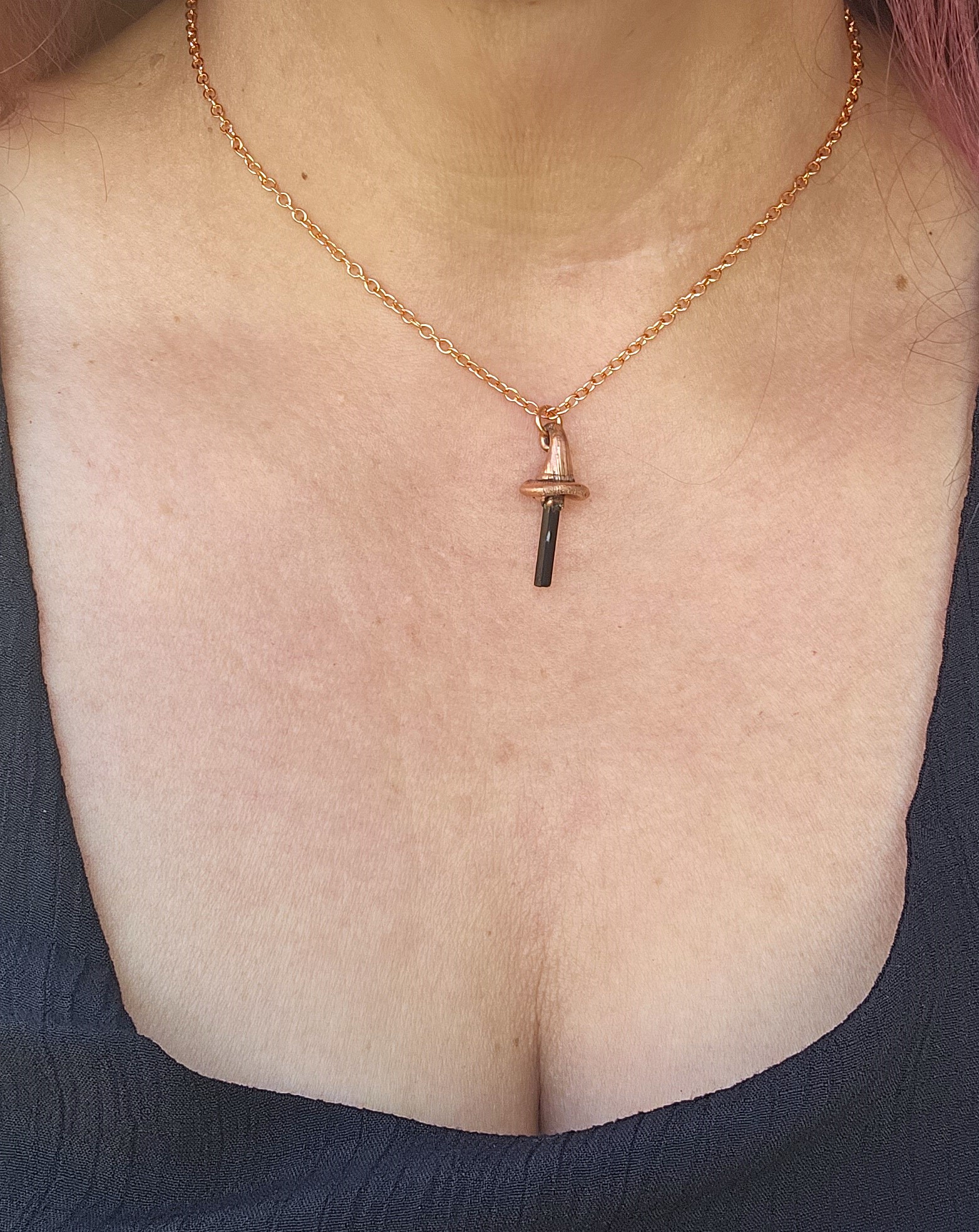 A model wearing the 1.25-inch Black Tourmaline Witch's Peak necklace. The copper pendant rests against a black garment, demonstrating the scale and how the 16-inch chain sits on the neckline.