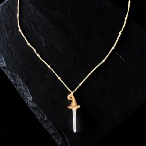 Close-up of a clear quartz crystal point set into a textured copper witch hat pendant. The image highlights the transparency of the crystal and the delicate rose gold beaded chain.