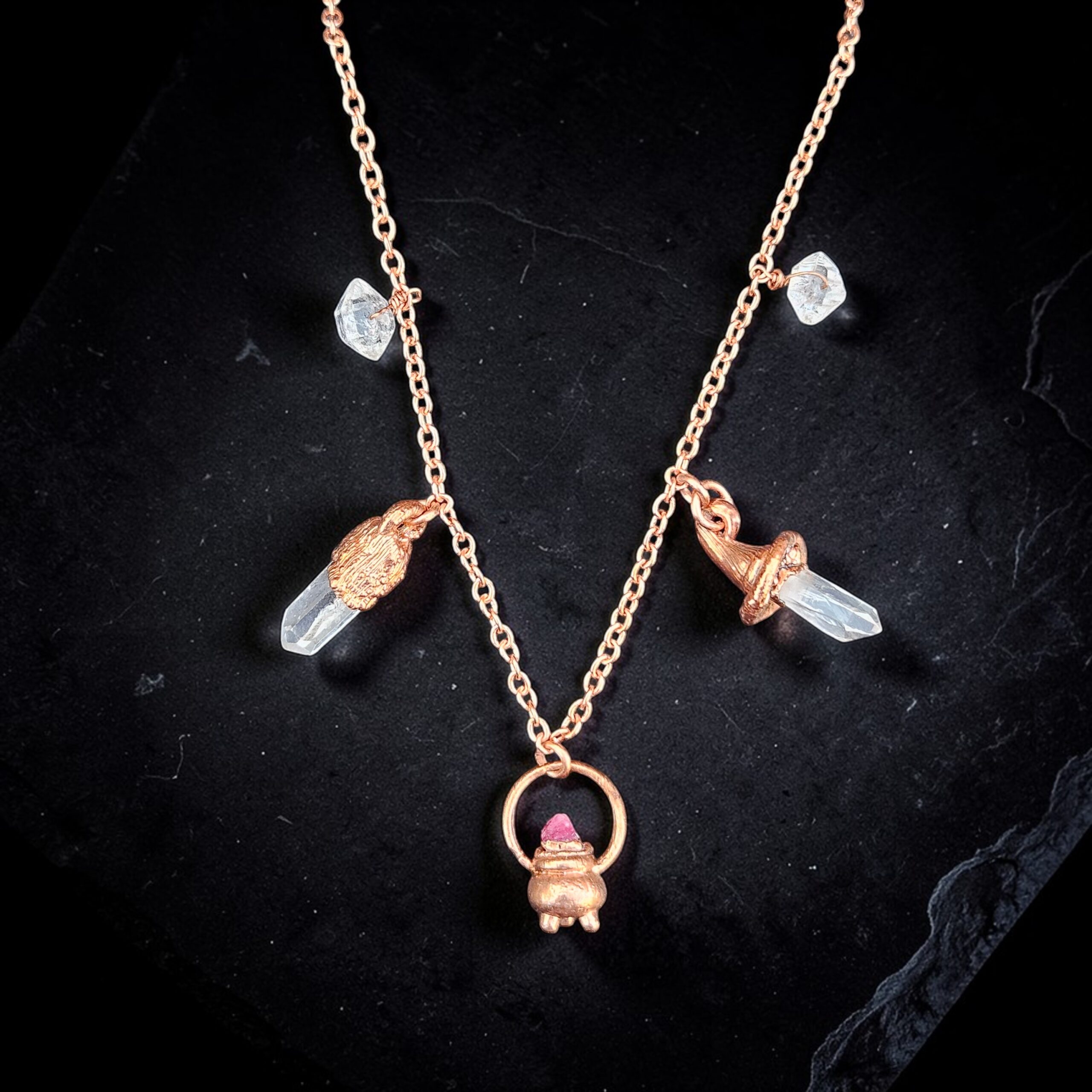 A copper charm necklace featuring a bubbling cauldron with pink spinel, herkimer diamonds, and clear quartz