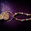 Macro close-up shot showcasing the fine details of the copper electroformed setting, highlighting the small garnet, iolite, and amethyst cabochons embedded at the neck loop, alongside the rich textures of the natural beaded strand.