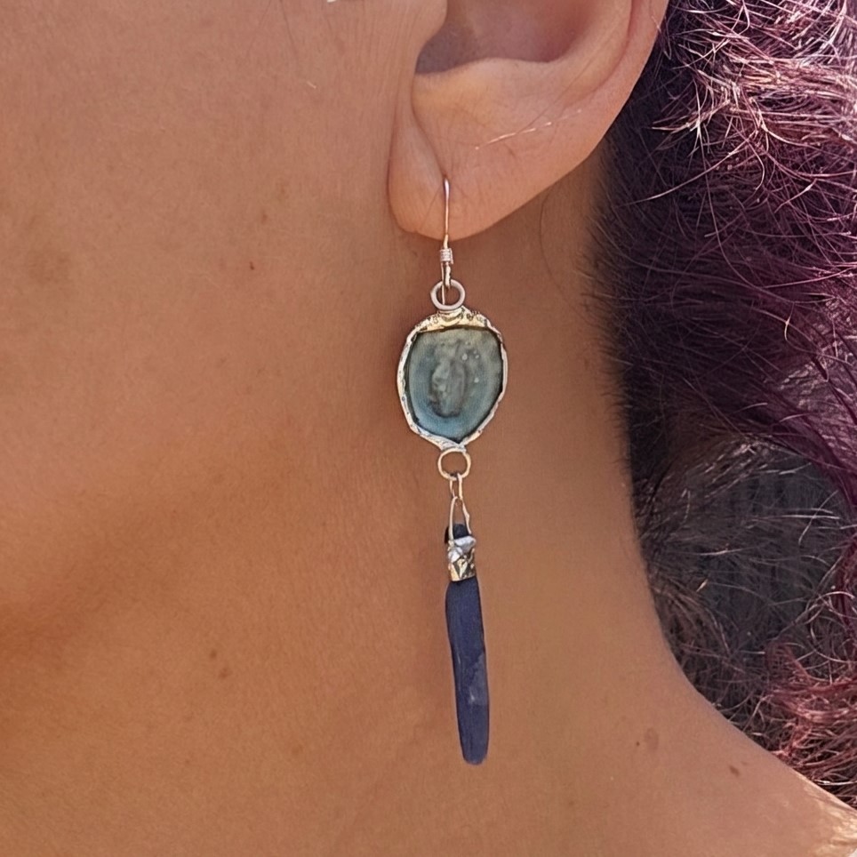 A close-up profile view of a model wearing the longer blue kyanite side of the pair, showing the elegant, dramatic 2.125-inch drop length and the slender, deep blue crystalline blade.