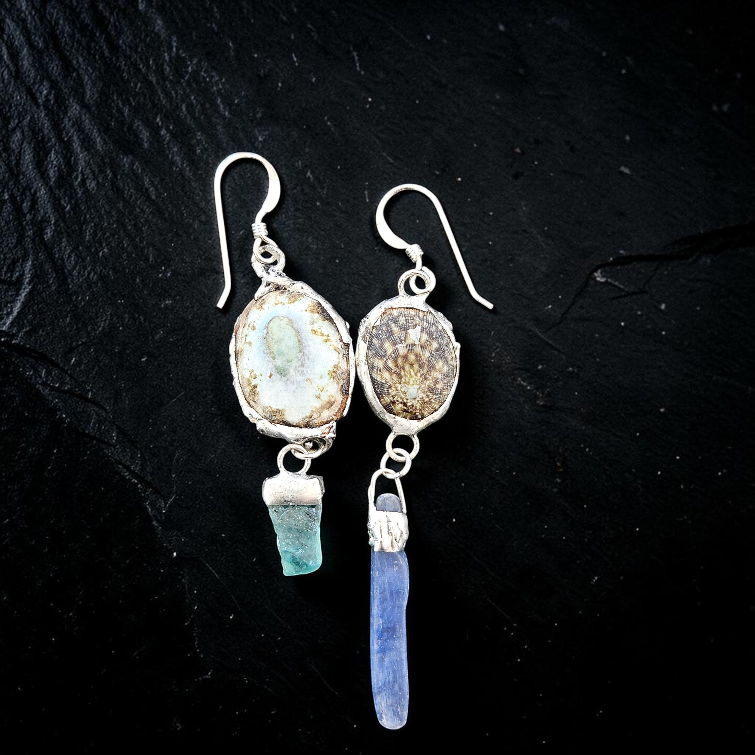 flat-lay photograph on a dark slate background showing the reverse side of the earrings, revealing the natural, rustic brown striated pattern of the genuine limpet shells bound in textured silver metalwork.