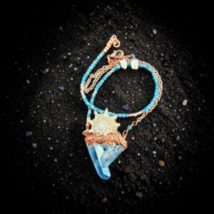 A gorgeous overhead shot of the talisman resting on shimmering black sand, highlighting the intense, iridescent turquoise flashes of the crystal points and the organic copper armor grown around the shell's spikes.