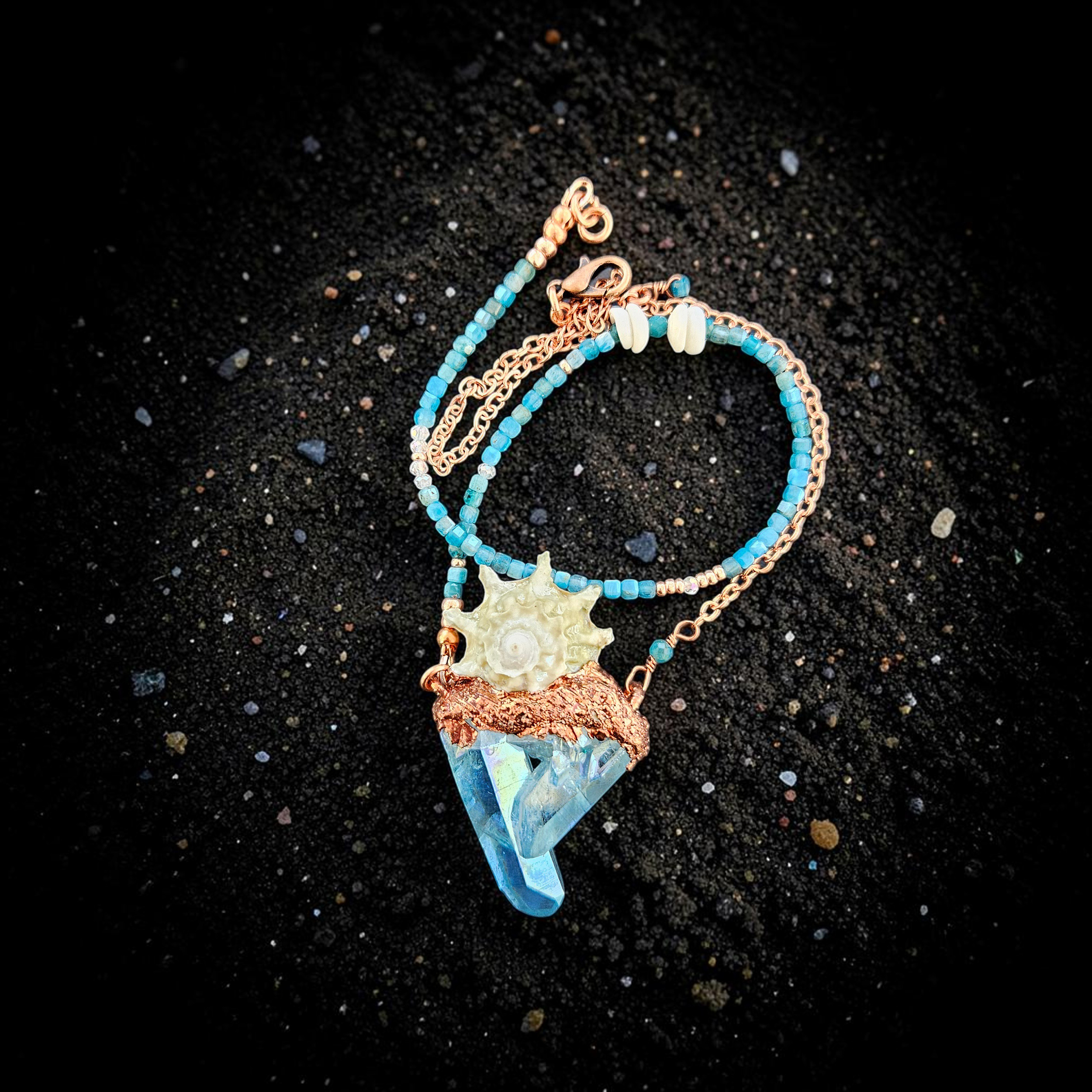 A gorgeous overhead shot of the talisman resting on shimmering black sand, highlighting the intense, iridescent turquoise flashes of the crystal points and the organic copper armor grown around the shell's spikes.