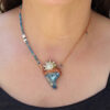A modeled view demonstrating the compact 2-inch drape of the aqua aura talisman against a black shirt, showing how the white vintage puka shells lay beautifully along the collarbone.