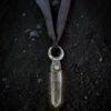 Overhead view of a large, 3-inch clear quartz crystal point topped with a copper electroformed crescent moon holding a shimmering abalone shell inlay. The pendant is suspended from a hand-dyed black silk ribbon with raw edges, laid flat on textured black sand.