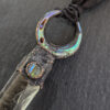 Macro close-up highlighting the vivid green, teal, and purple iridescence of the abalone shell crescent moon and matching round cabochon. The copper setting features a dark, heavily cratered, textured patina.