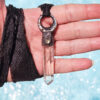 A hand-held shot under bright sunlight, demonstrating the incredible water-clear transparency of the 3-inch natural quartz point and how the adjustable black silk ribbon wraps around the hand.
