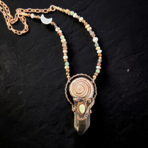 A hand-grown copper electroformed pendant featuring a long smoky quartz crystal point crowned with a spiral sundial shell and a milky opal cabochon. The piece is suspended from a 17-inch mixed accent bead and copper link chain.