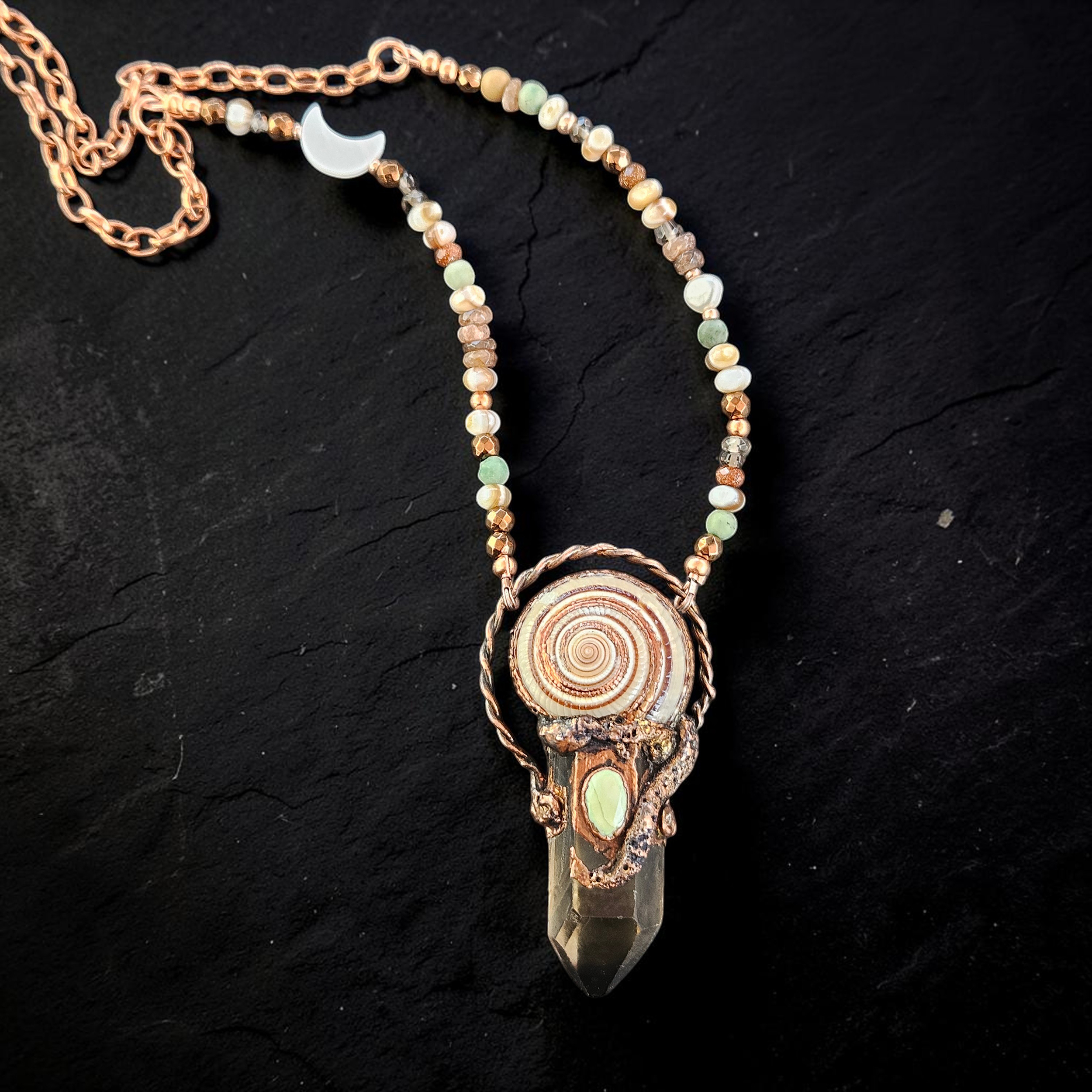 A hand-grown copper electroformed pendant featuring a long smoky quartz crystal point crowned with a spiral sundial shell and a milky opal cabochon. The piece is suspended from a 17-inch mixed accent bead and copper link chain.
