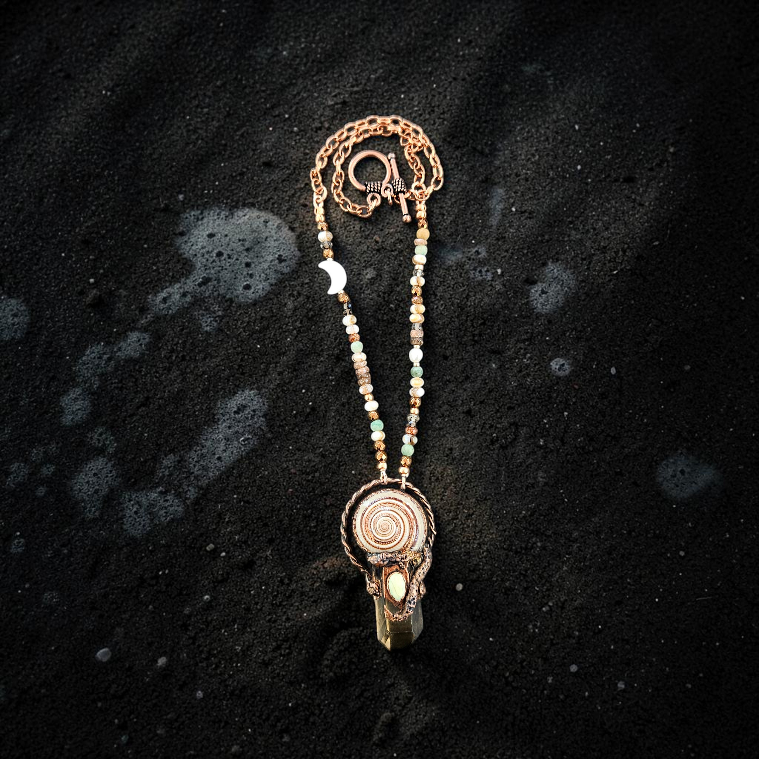 A wide overhead product photo showcasing the entire 17-inch necklace laid out on black sand, detailing the transition from the earthy gemstone bead strand to the sturdy copper link chain and toggle clasp.