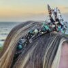 A left profile close-up showing how the textured, barnacle-like electroformed copper band of the crown wraps securely around the side of a blonde model's hair, highlighting embedded high-luster pearls and raw stones.
