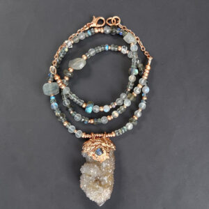 Flat lay of a quartz druzy pendant with labradorite on a chain of labradorite and moonstone with copper accents.