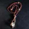 Hand-knotted garnet bead necklace with a copper electroformed boxwood branch pendant cradling a clear quartz crystal point and garnet accents on a dark slate background.