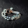 Artistic close-up of the coiled aquamarine and silver chain with the raw clear quartz point pendant resting on black slate under focused light.