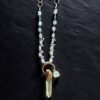 Artistic close-up of the coiled aquamarine and silver chain with the raw clear quartz point pendant resting on black slate under focused light.