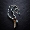 Flat lay view of the Luminous Depths necklace coiled neatly on black slate, highlighting the sterling silver circle links, blue bead details, and raw aquamarine gem strand.