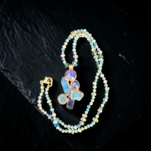 Hand-knotted blue and green gemstone bead necklace coiled on black slate around an electroformed copper cluster pendant featuring aqua aura quartz, lapis lazuli, and blue kyanite, with a 14k gold-filled lobster clasp.