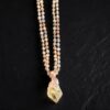 Detailed view of the golden rutile needles inside the quartz point pendant and the smoky rose, olive, and champagne tones of the hand-knotted tourmaline beads on black slate.