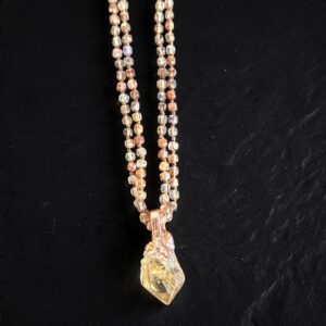 Detailed view of the golden rutile needles inside the quartz point pendant and the smoky rose, olive, and champagne tones of the hand-knotted tourmaline beads on black slate.
